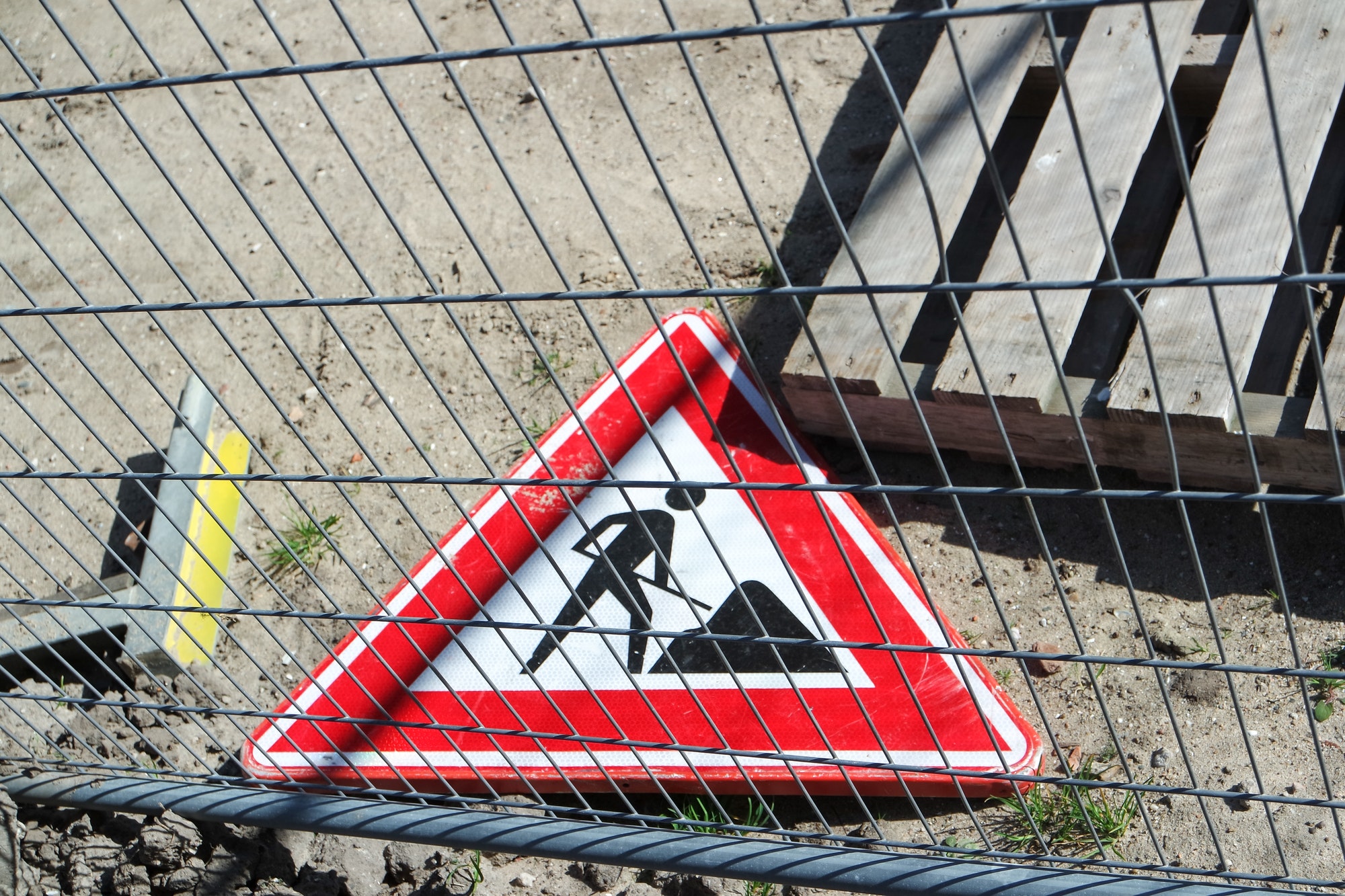 Road sign. Work in progress. Laying on the ground and behind the fence.